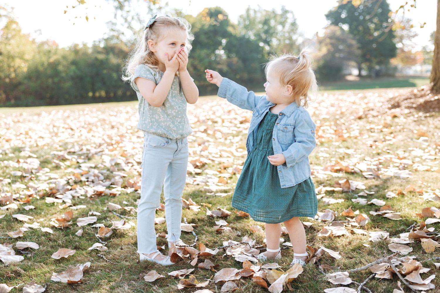 Children playing together in a pile of colorful autumn leaves during a golden sunset in the park.