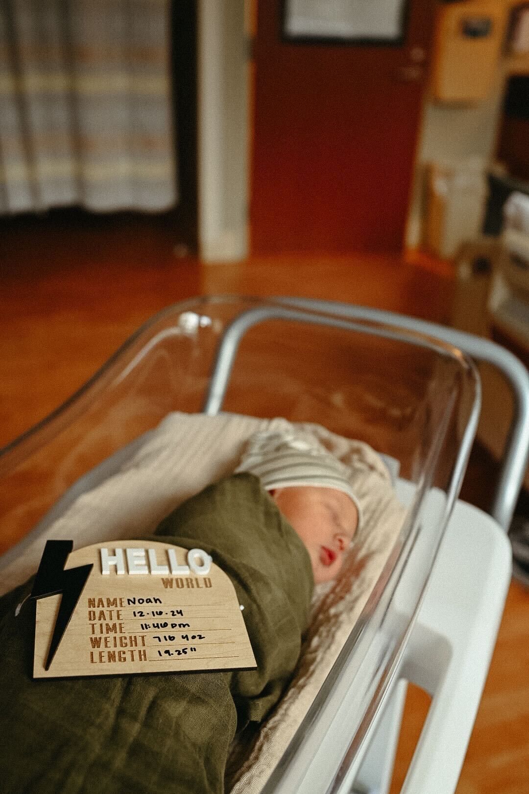 Newborn rests in hospital bassinet with identification card visible.