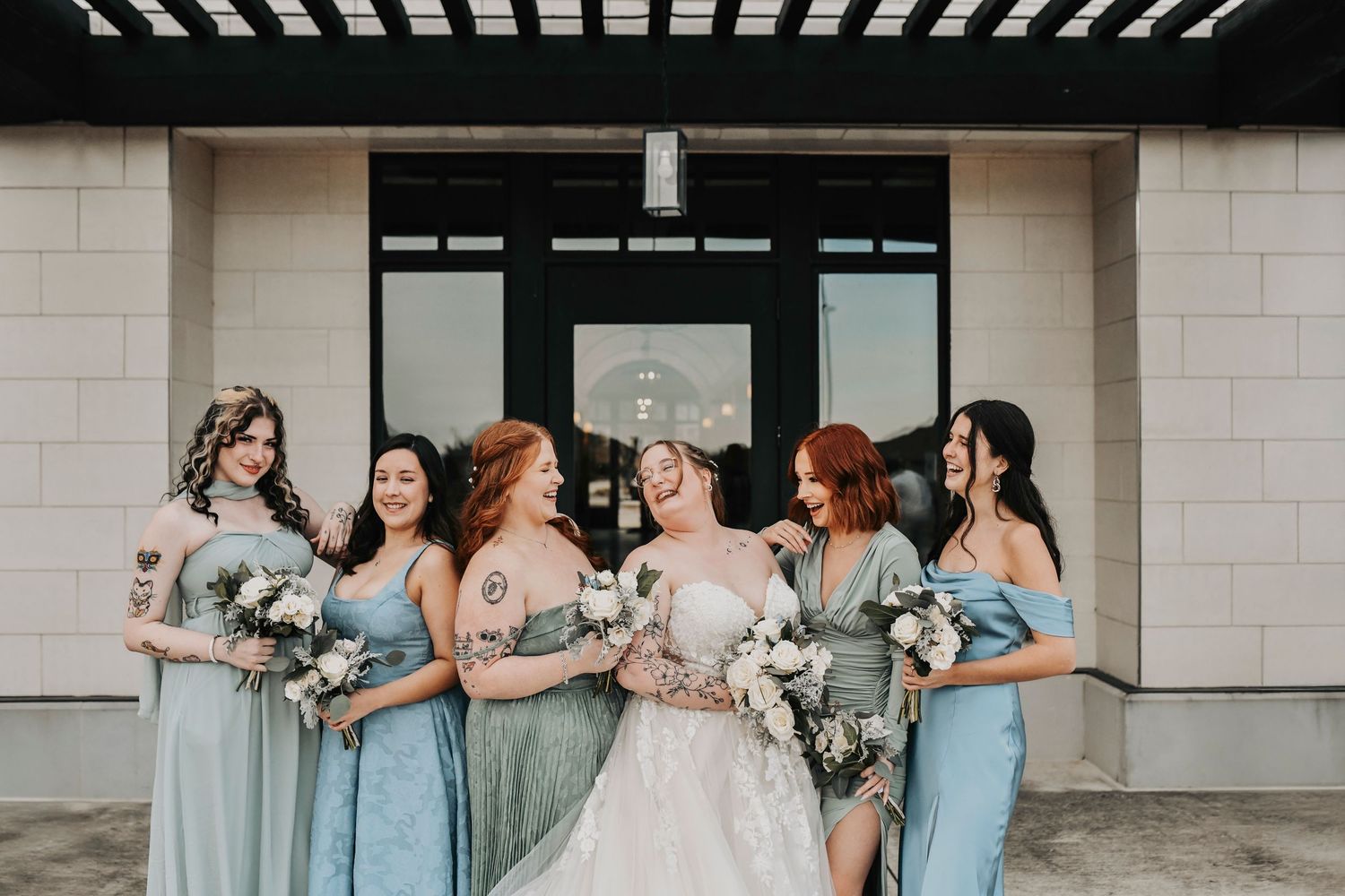Mixed and matched bridesmaids wearing powder blue and sage dresses for a winter wedding