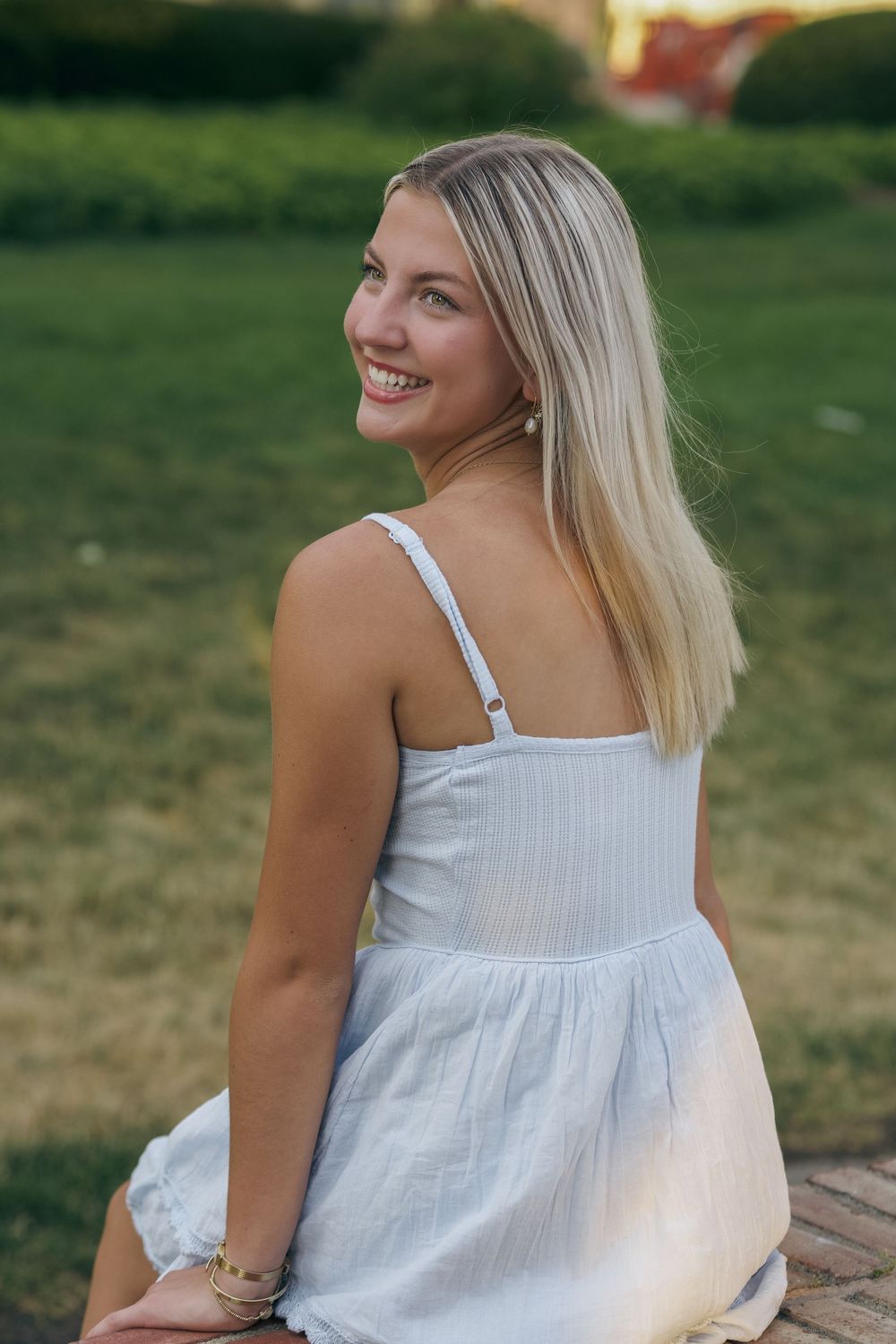 Woman in white summer dress sitting outdoors on a sunny day with natural greenery in background.