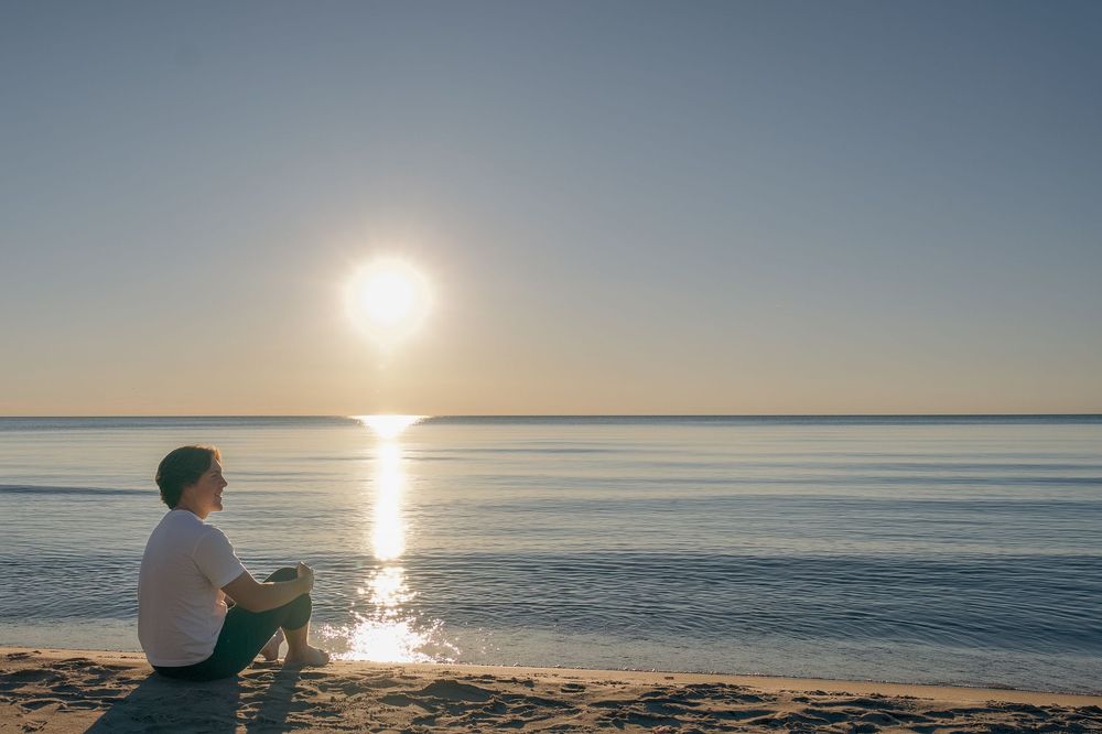 A serene sunset over the ocean horizon creates a golden glow across the tranquil water's surface.