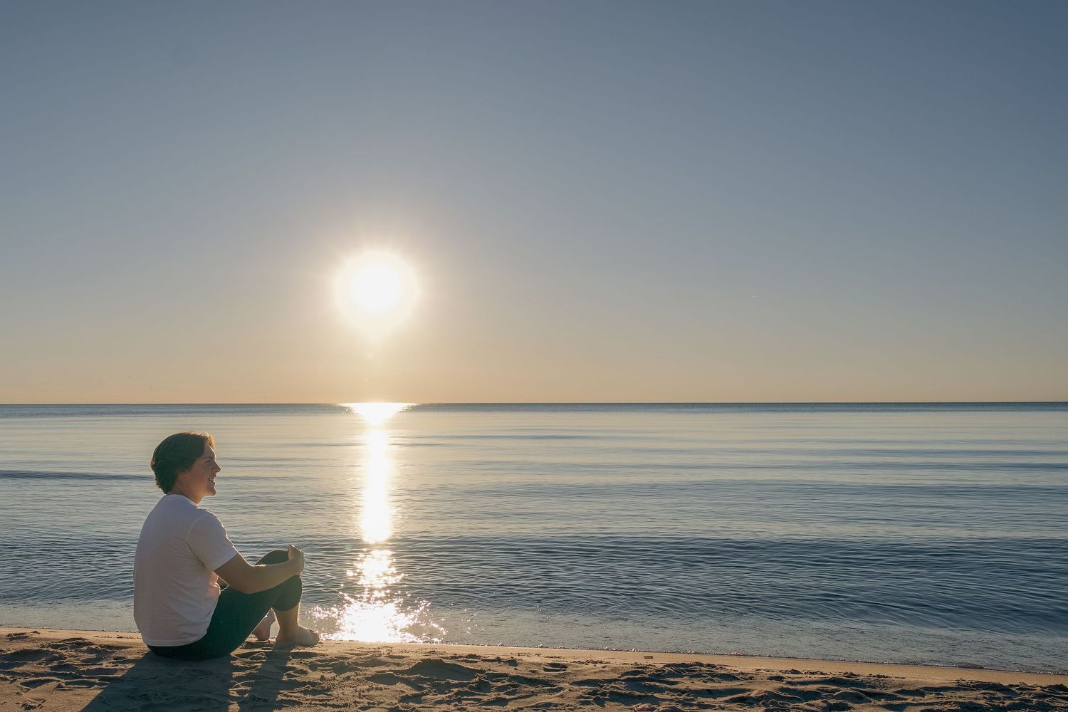 A serene sunset over the ocean horizon creates a golden glow across the tranquil water's surface.