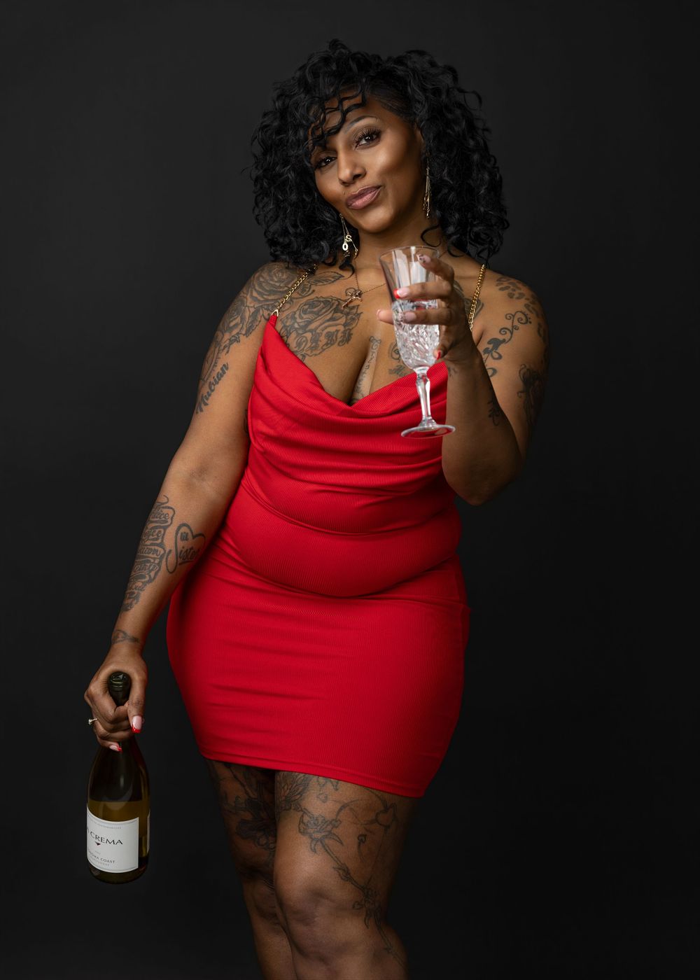 Person in a red tank top poses with tattoos against dark background while holding toilet paper and wine bottle.