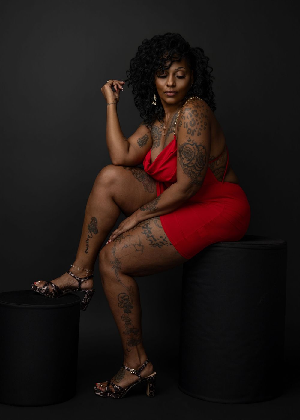 A woman in a red dress poses artistically on black blocks against a dark background, showcasing elegant leopard print heels.