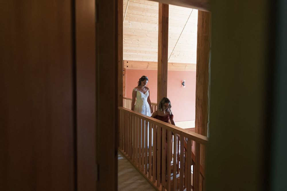 Bride and bridesmaid on a wooden balcony inside a rustic wedding venue.