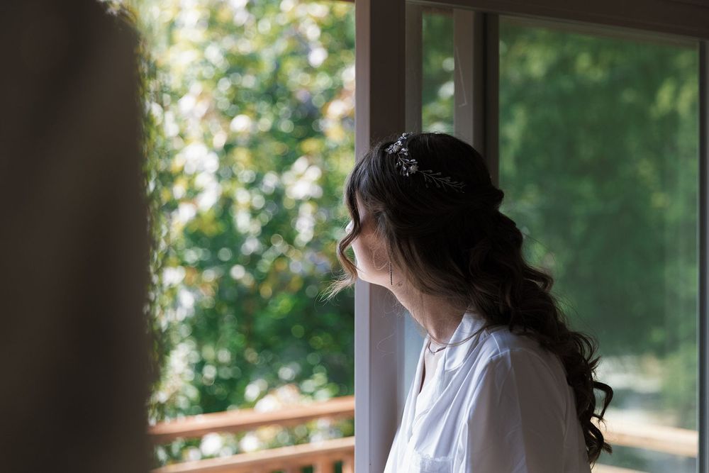Bride with floral hair accessory gazing out a window on her wedding morning.