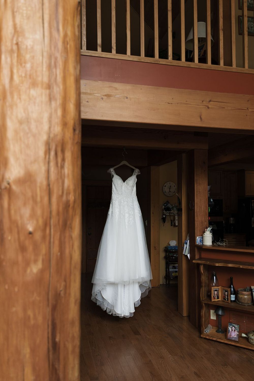 Elegant white lace wedding dress hanging in a rustic wooden cabin interior.