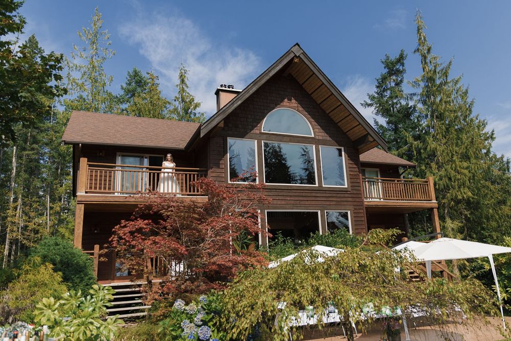 Rustic wooden chalet-style home surrounded by tall evergreen trees with large picture windows.