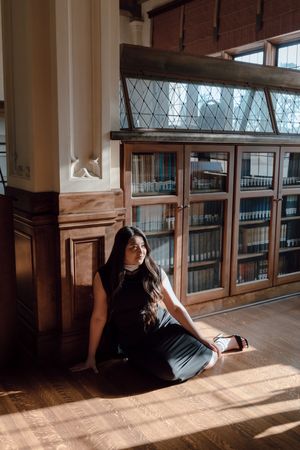 Graduate sits on the library floor during her grad photoshoot at the University of San Francisco. By Bay Area Graduation Photographer.