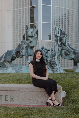Graduate sits in front of sculpture at the University of San Francisco. By Bay Area Graduation Photographer.