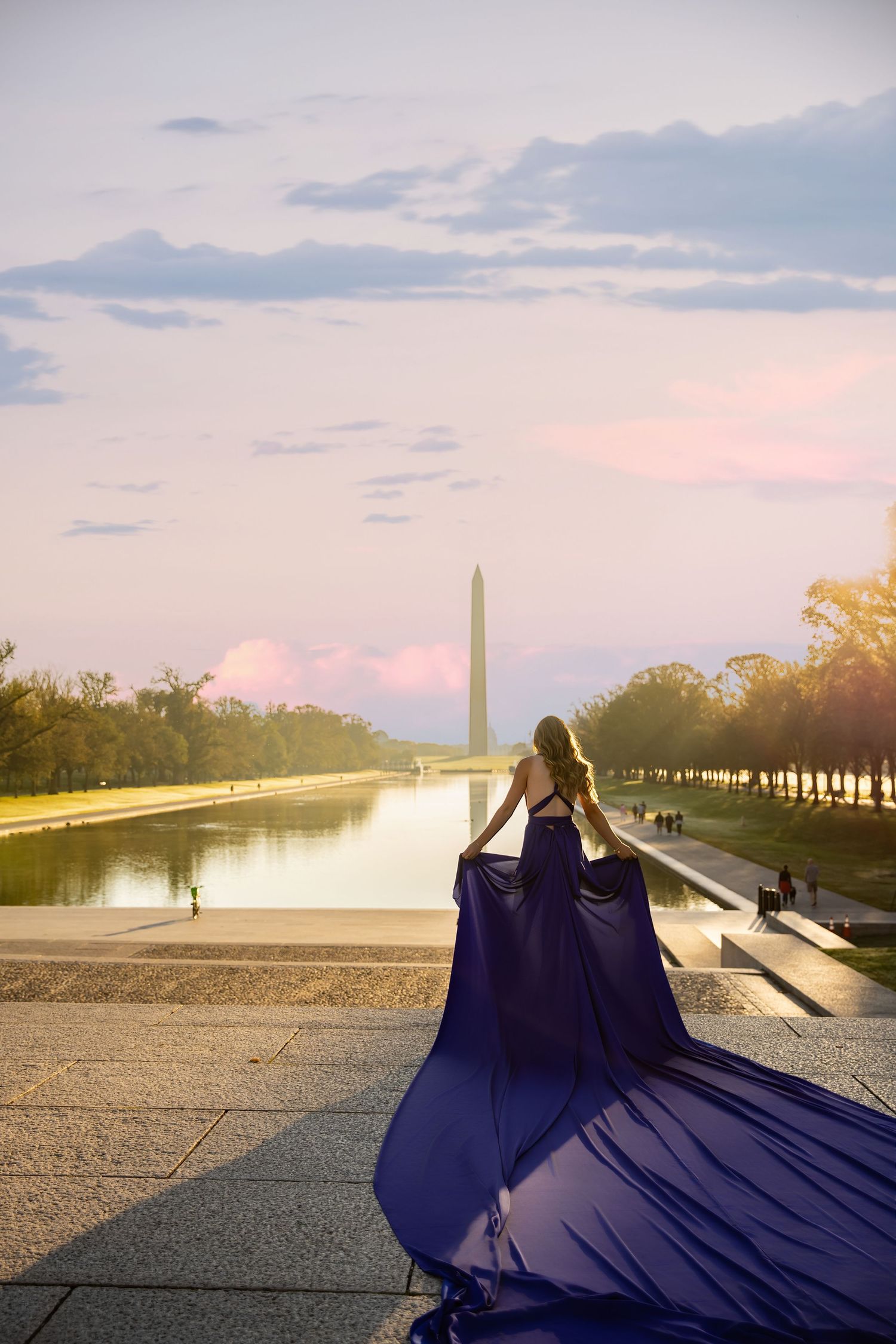 A person in a flowing navy blue gown poses at the Lincoln Memorial Reflecting Pool during sunset in Washington DC. Flying Dress Photoshoot