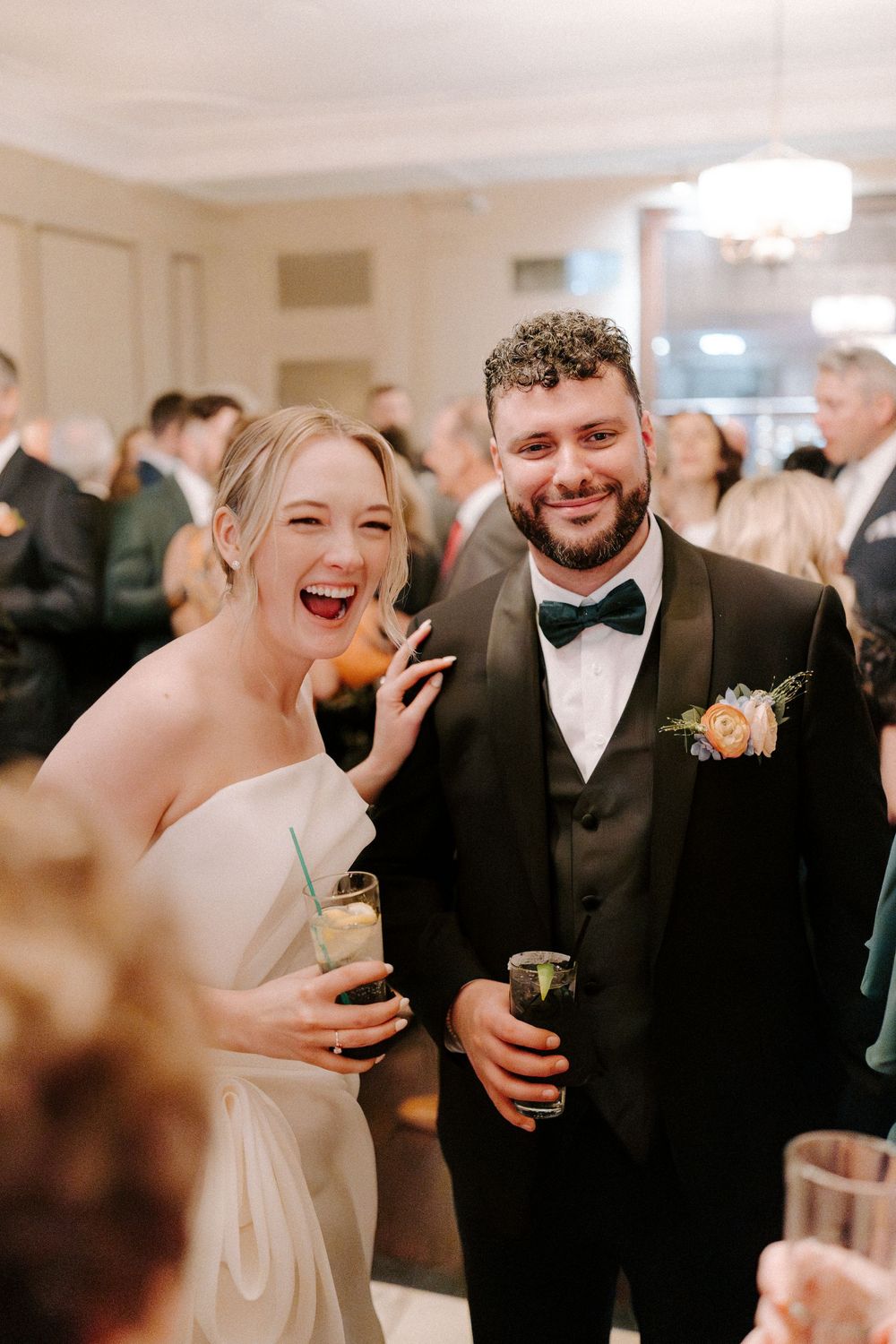 A candid moment of joyful laughter shared between guests at an elegant wedding reception in a bright indoor venue.