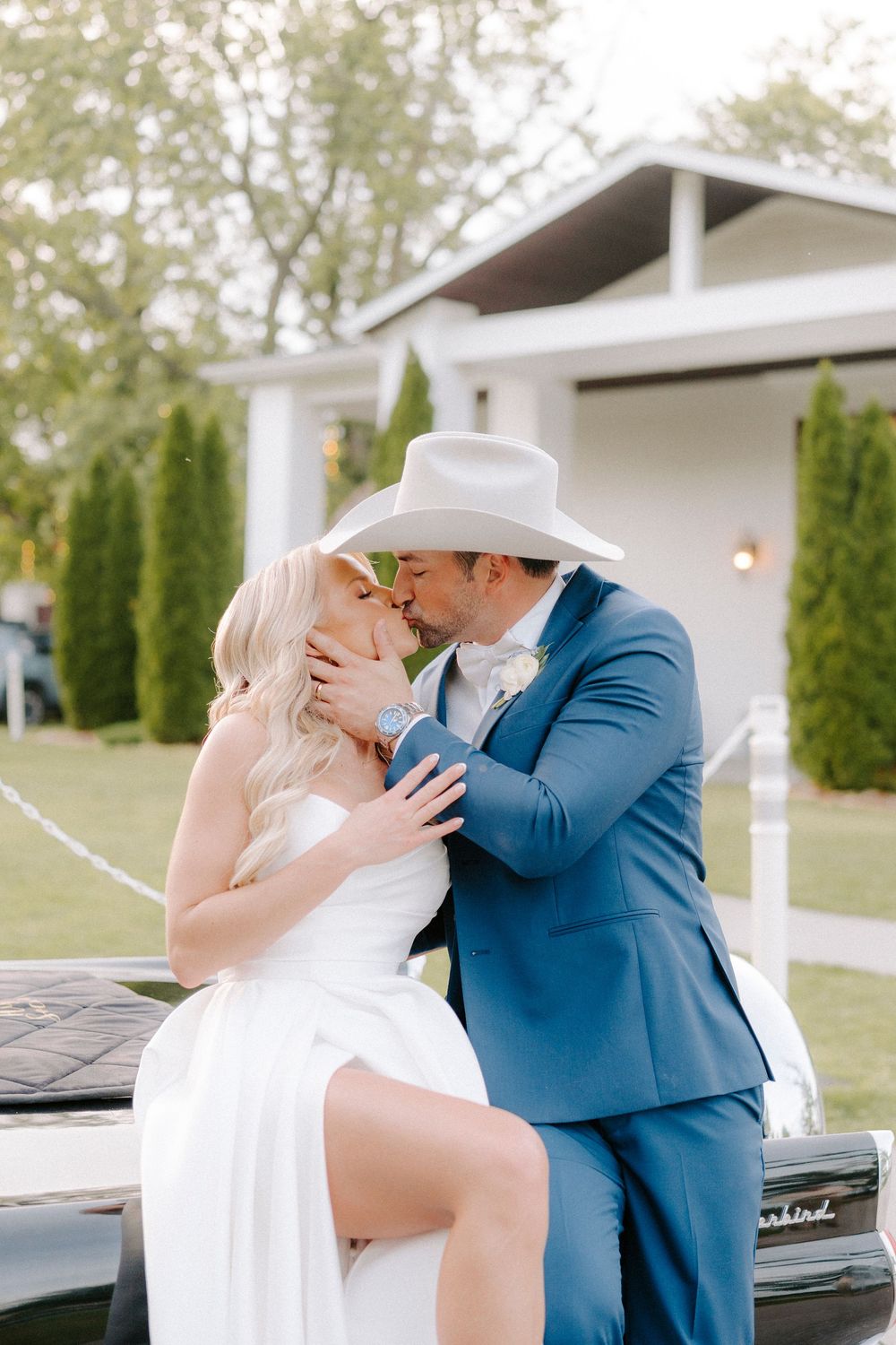 A romantic moment captured between a couple in formal wedding attire sharing a kiss outdoors.