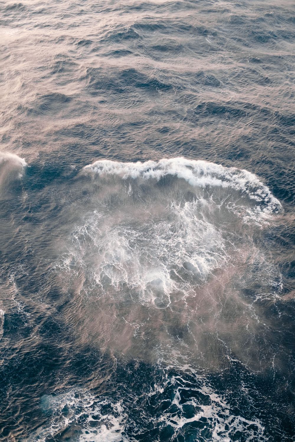 Aerial view of turbulent ocean waves with white sea foam swirling on deep blue water surface.