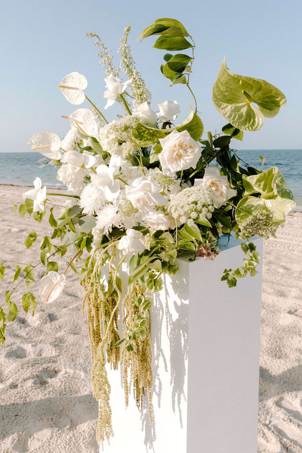White floral beach wedding arrangements with delicate blooms and greenery against a sandy backdrop.
