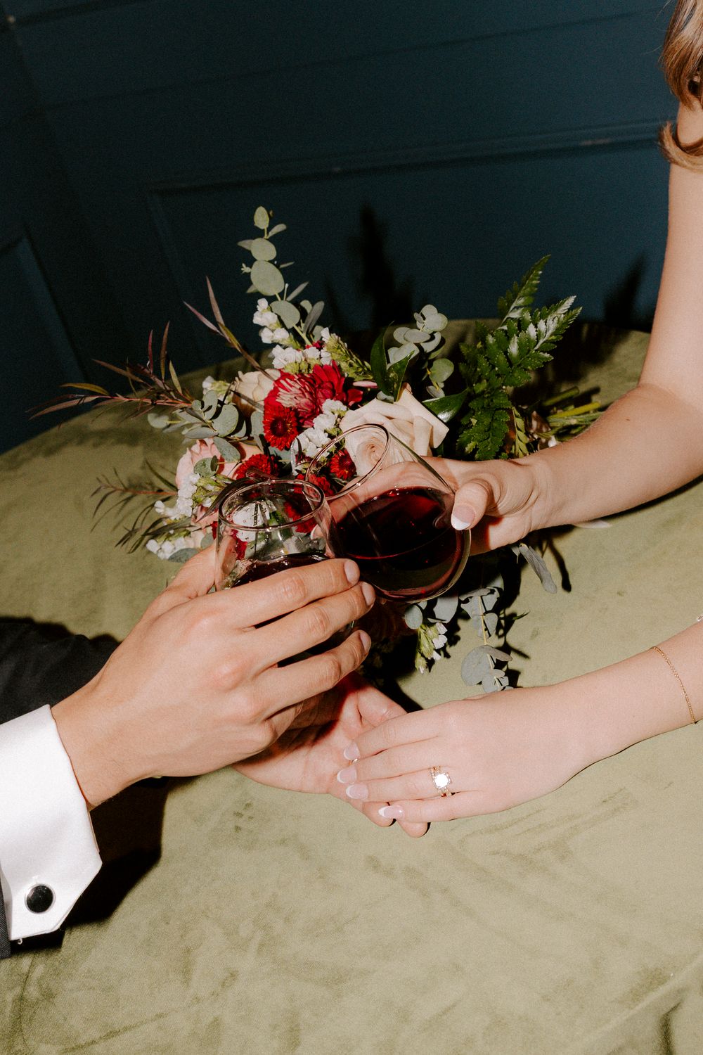 Hands exchanging delicate floral bouquets with red and white flowers against a neutral background.