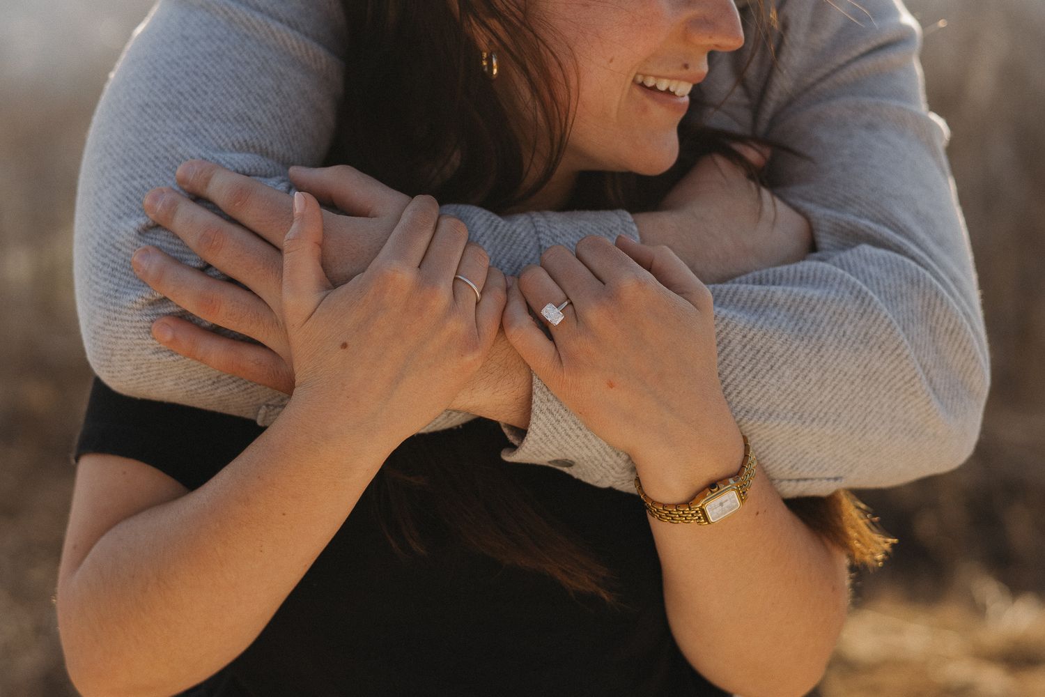 Close-up of a couple embracing, woman wearing an engagement ring and gold bracelet.