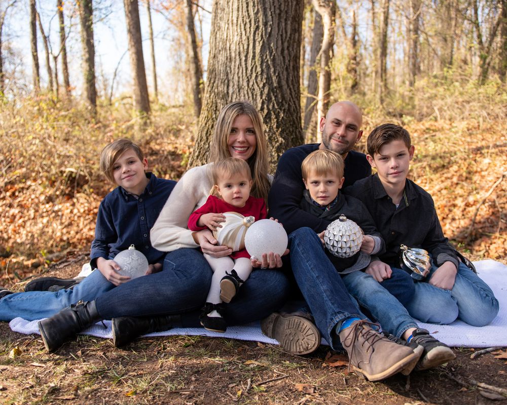 A family sits together on a blanket in an autumn forest setting wearing coordinating winter outfits.