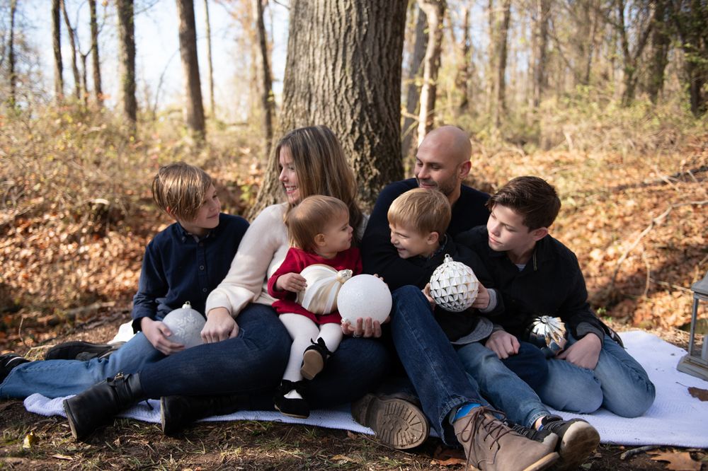 A family cuddles together and smiles while sitting on a blanket surrounded by fall foliage.