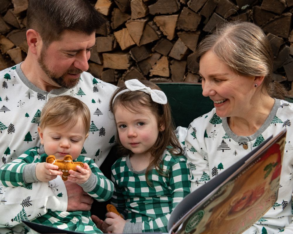 A family reads together while wearing matching winter pajamas next to a woodpile.