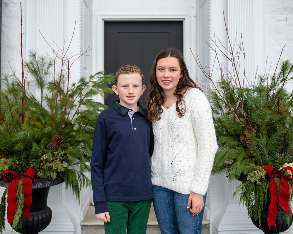 Holiday scene with decorated greenery and red bows framing a white doorway entrance.