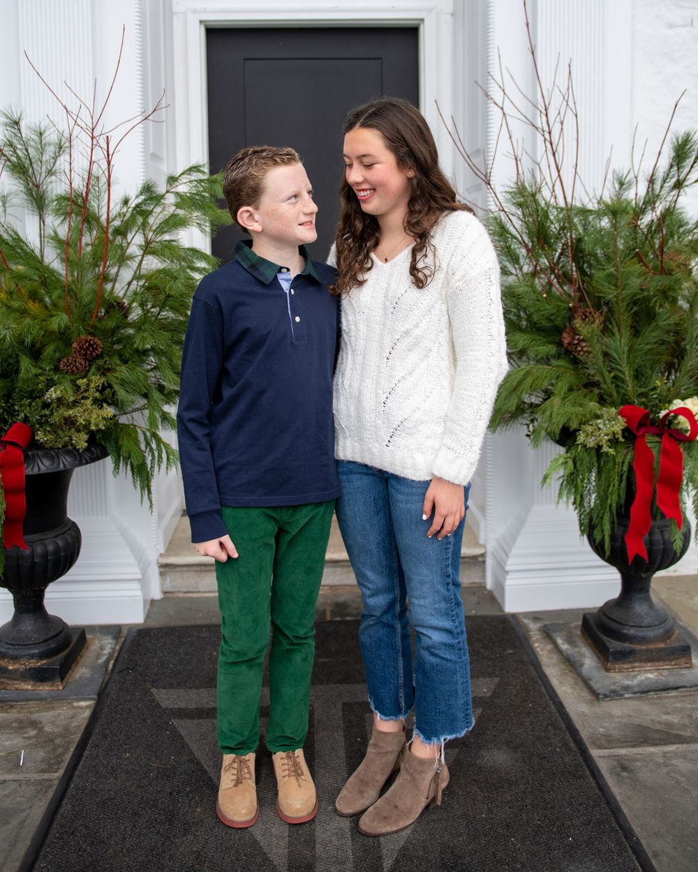 Two people pose in front of a white door decorated with holiday greenery and red bows.