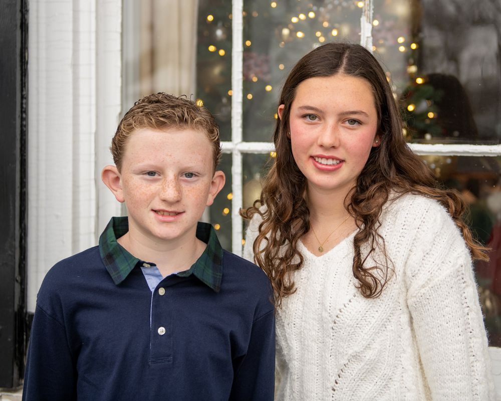 Indoor holiday portrait with twinkling lights visible through a window in the background.