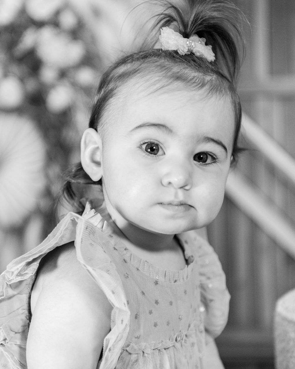 Baby in light dress poses for black and white portrait.