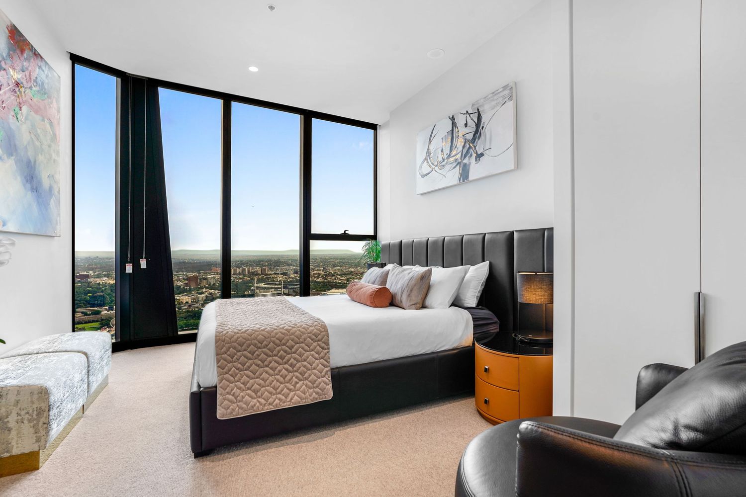 Luxurious bedroom with floor-to-ceiling windows offering panoramic city views and contemporary furnishings.