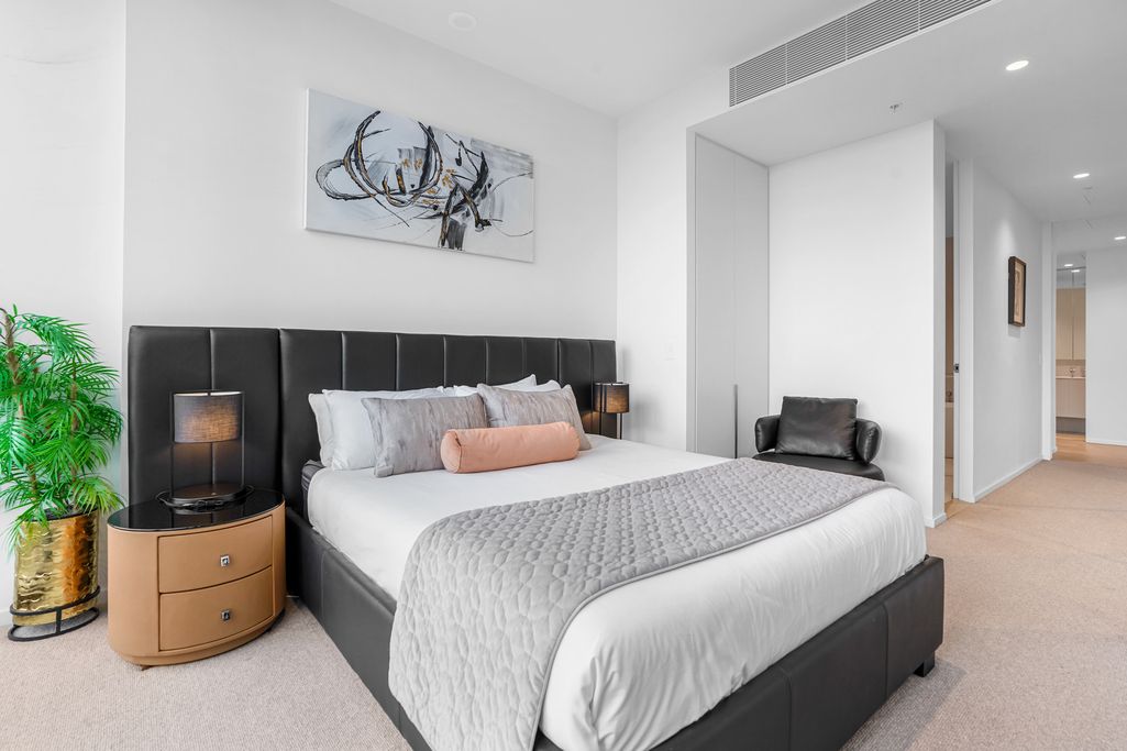 Modern bedroom with grey bedding, abstract wall art, and wooden side tables.