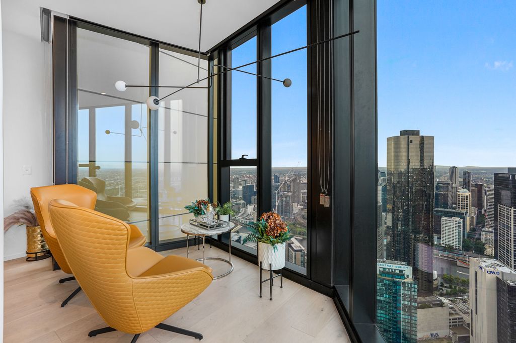 Luxury apartment corner lounge area with yellow accent chair and panoramic city views through floor-to-ceiling windows.