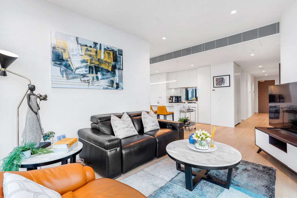 Contemporary living room with black leather couch, orange accents, and abstract wall art.