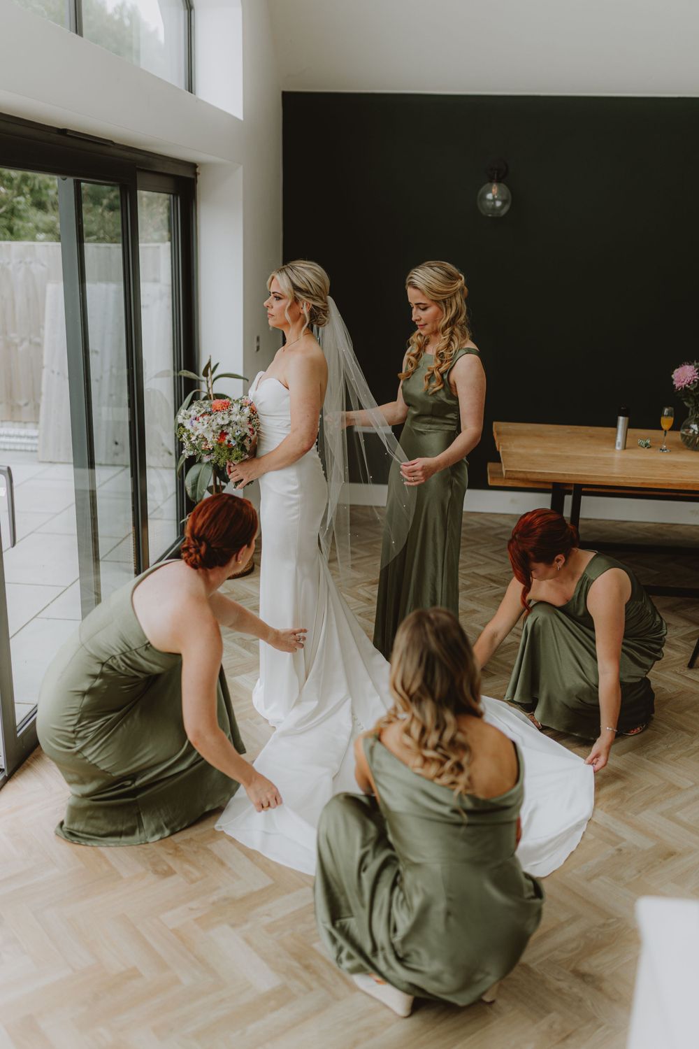 Wedding preparation scene with attendants helping adjust a white wedding gown.