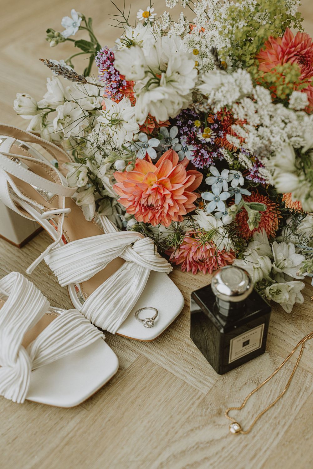 Wedding details featuring white tassel sandals and colorful floral arrangements on a wooden surface.