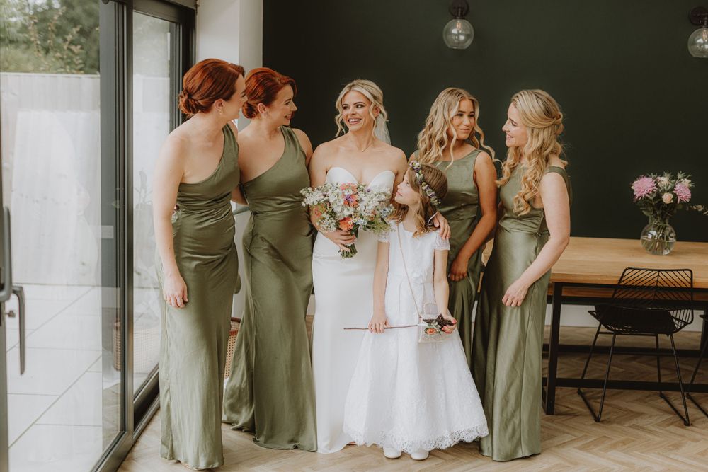 Wedding party in sage green dresses and white gowns lined up for photos.
