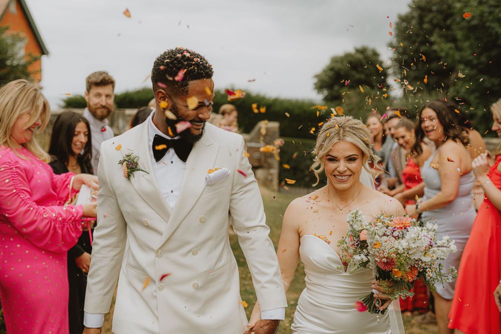 Joyful wedding party celebration outdoors with colorful attire and floral bouquets.