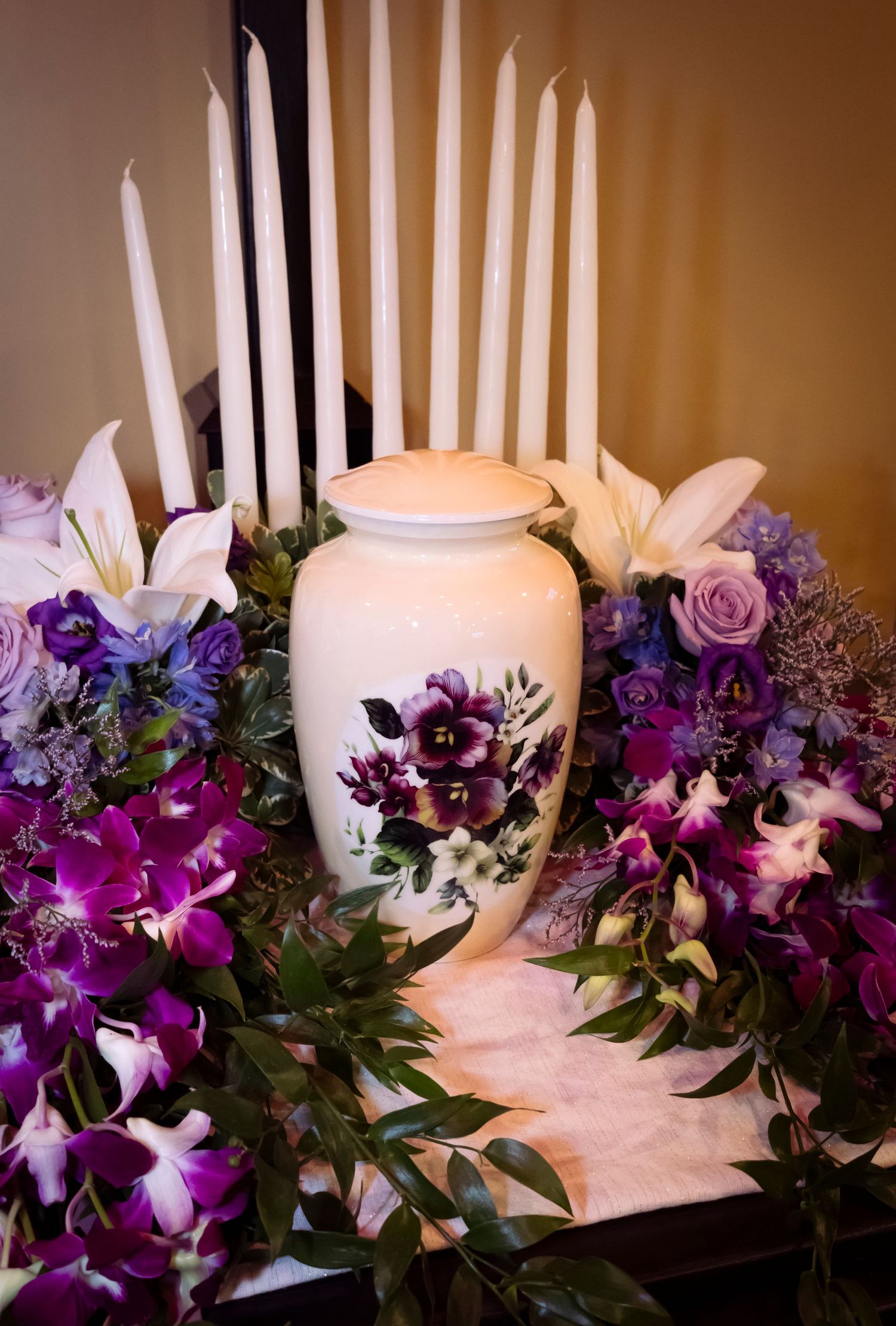 Urn photo surrounded by different types of purple flowers and candles