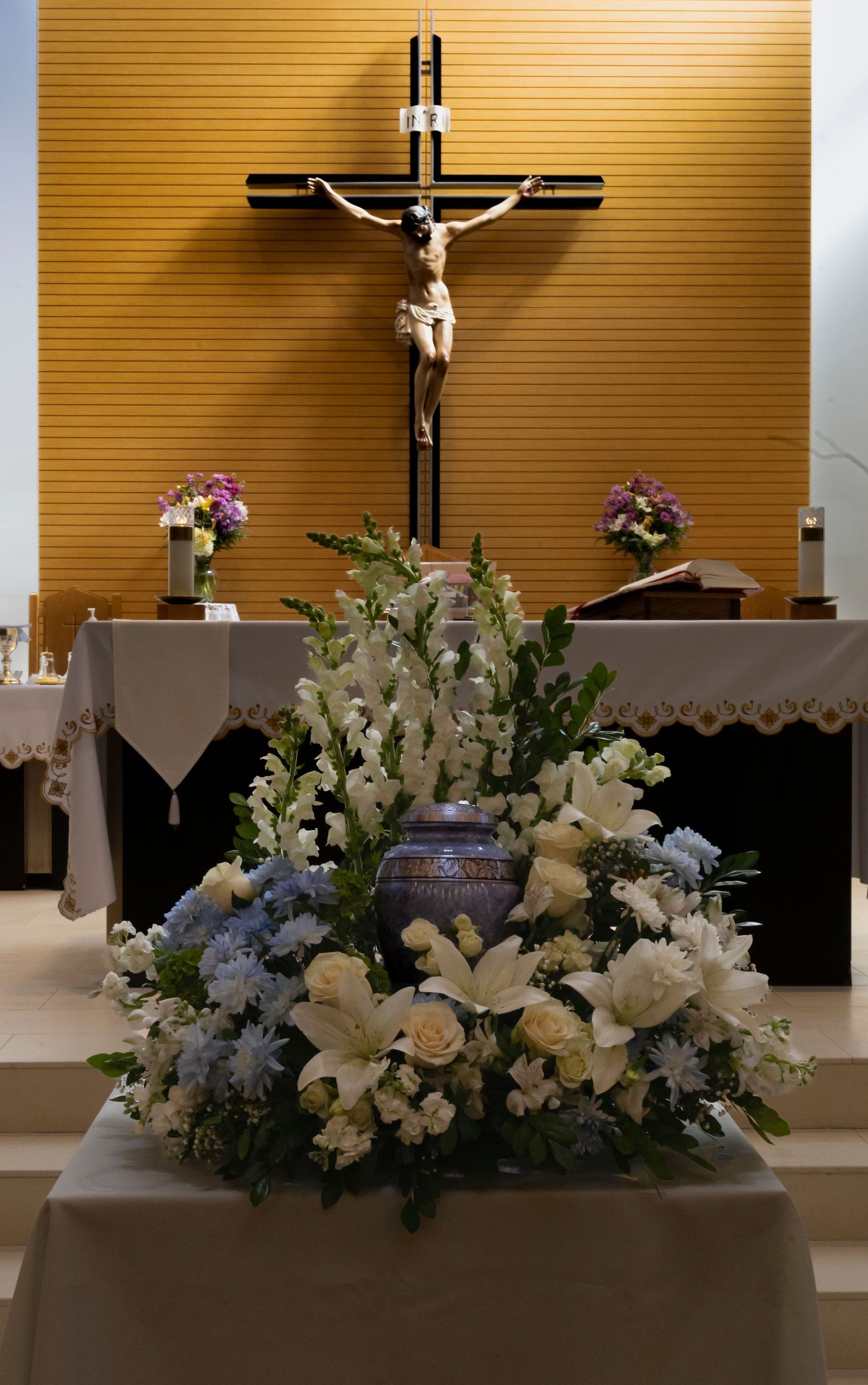 Photo of urn surrounded by white flowers underneath Jesus on the cross