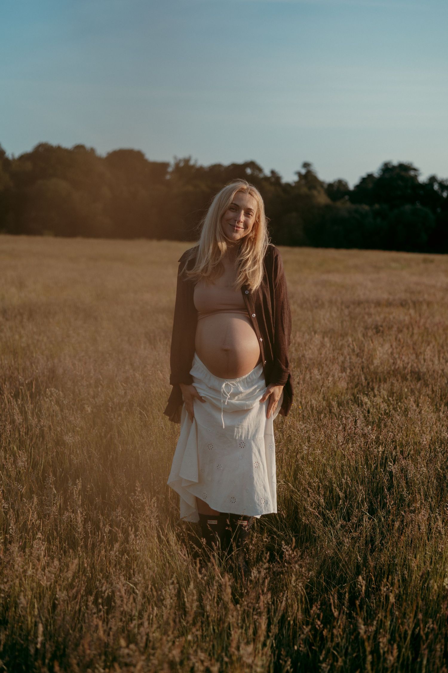 Atmospheric maternity photography in a golden wheat field at sunset.