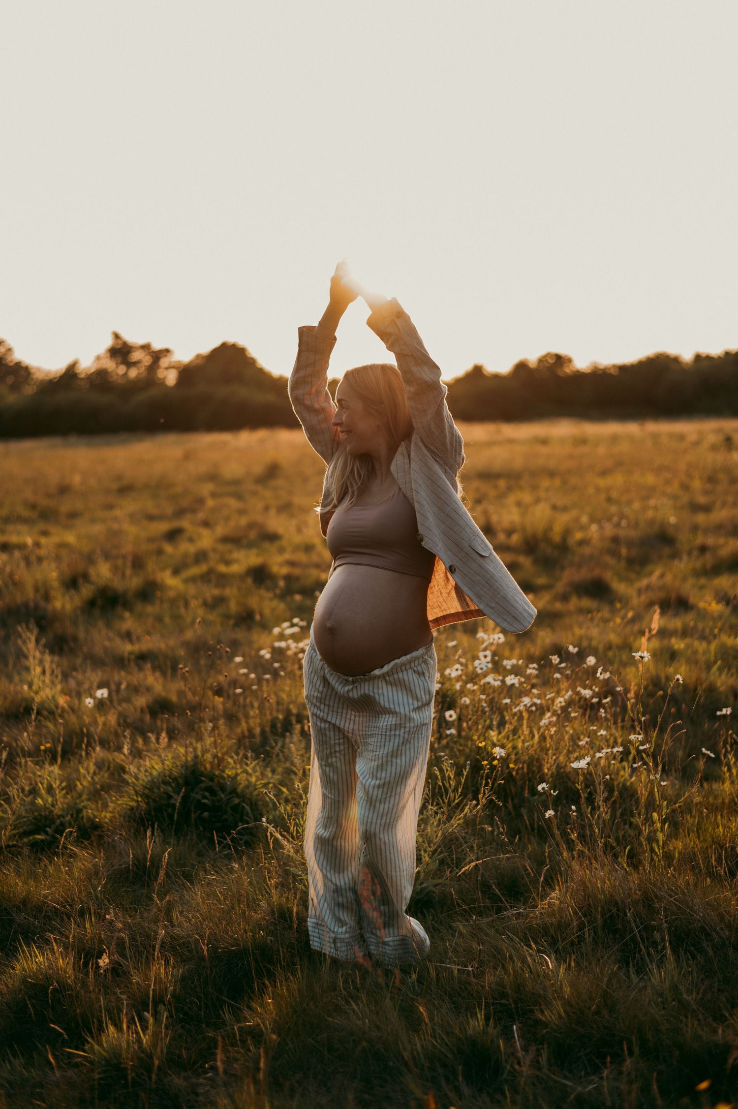 Candid maternity poses captured in a sun-drenched field during golden hour.