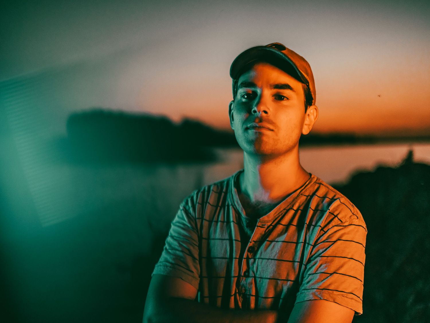 Portrait of a person in striped shirt against dramatic sunset backdrop.