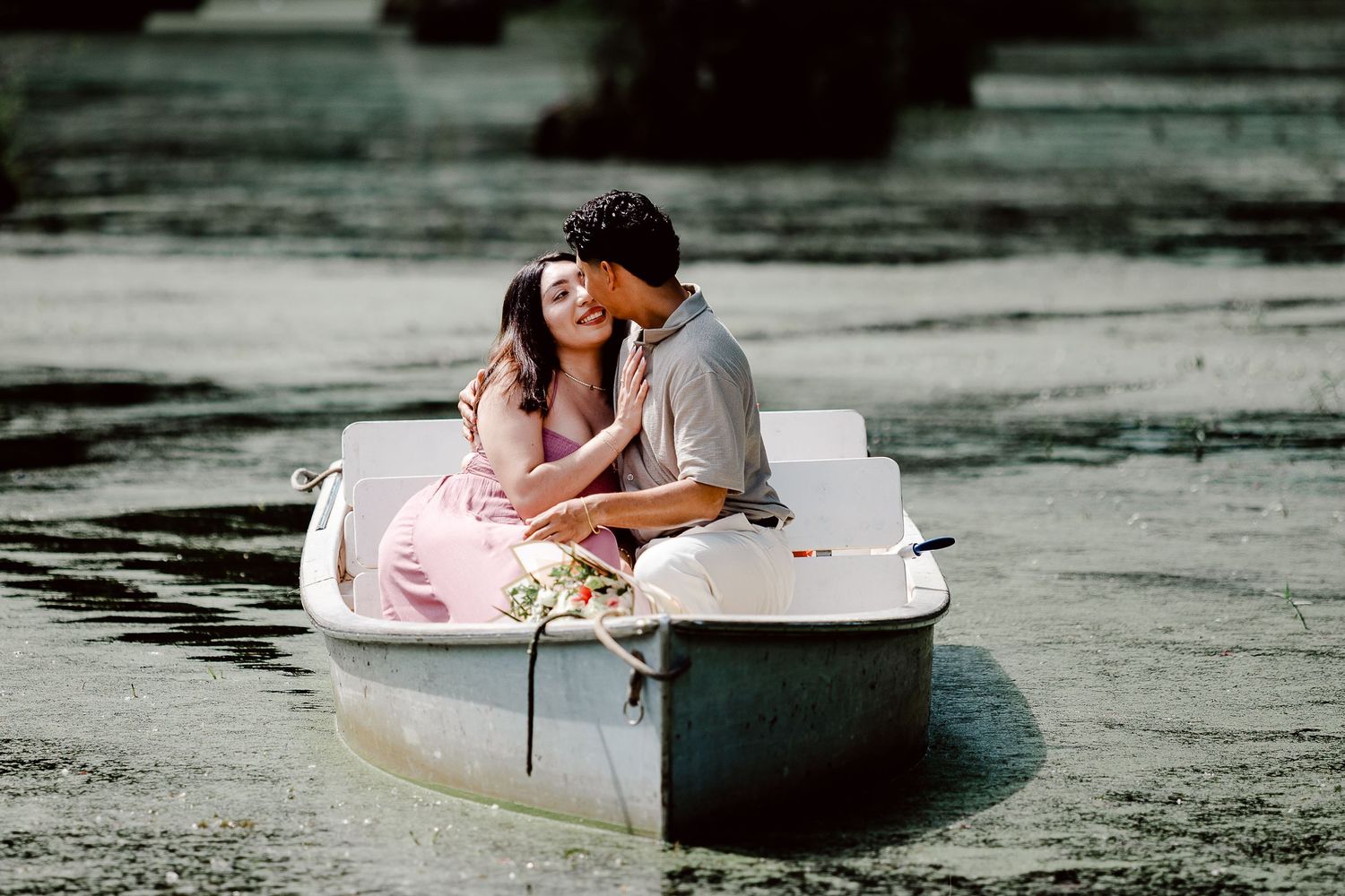 A couple shares an intimate moment while sitting in a small rowboat on dark reflective water.