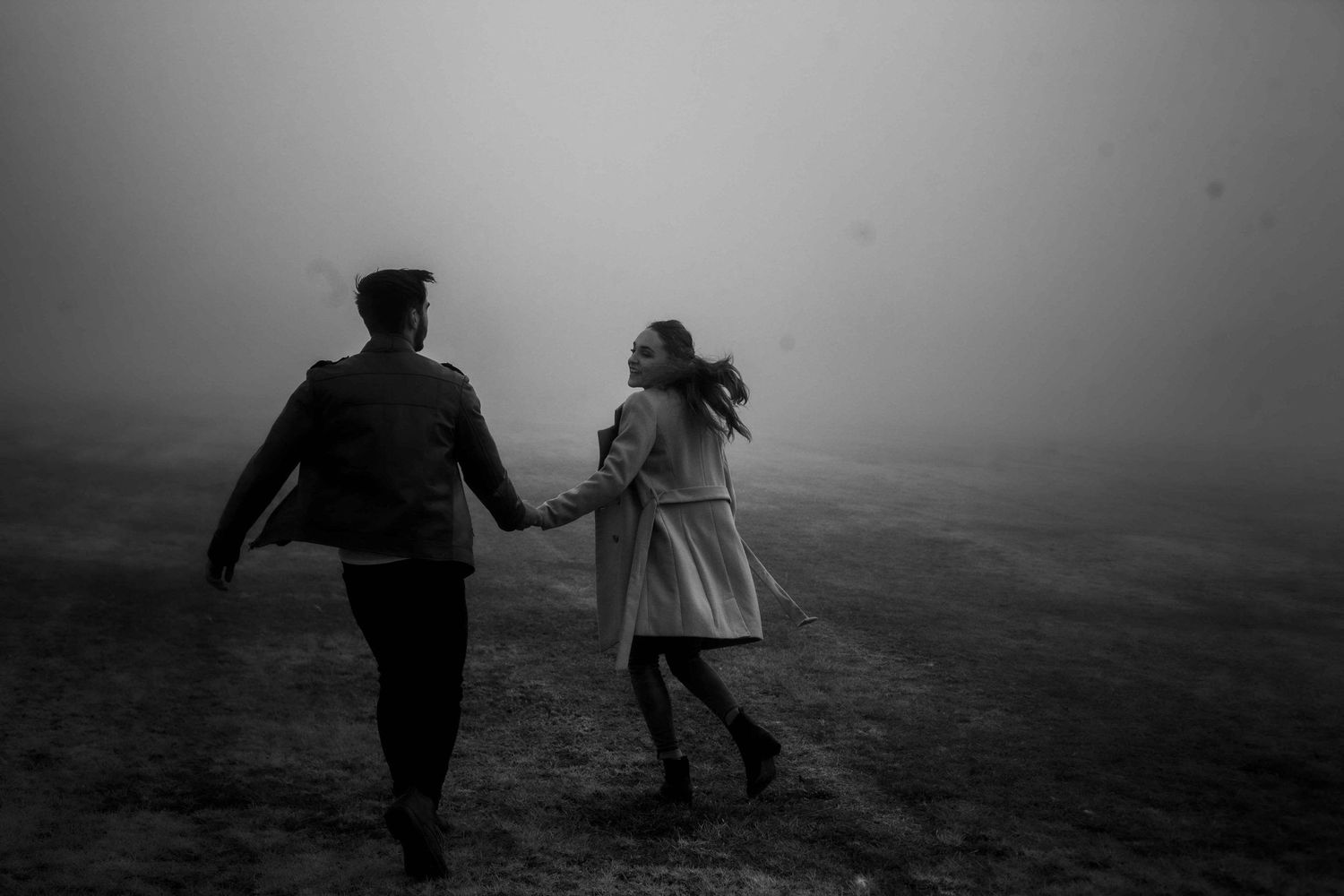 A couple running hand in hand through misty terrain in black and white.