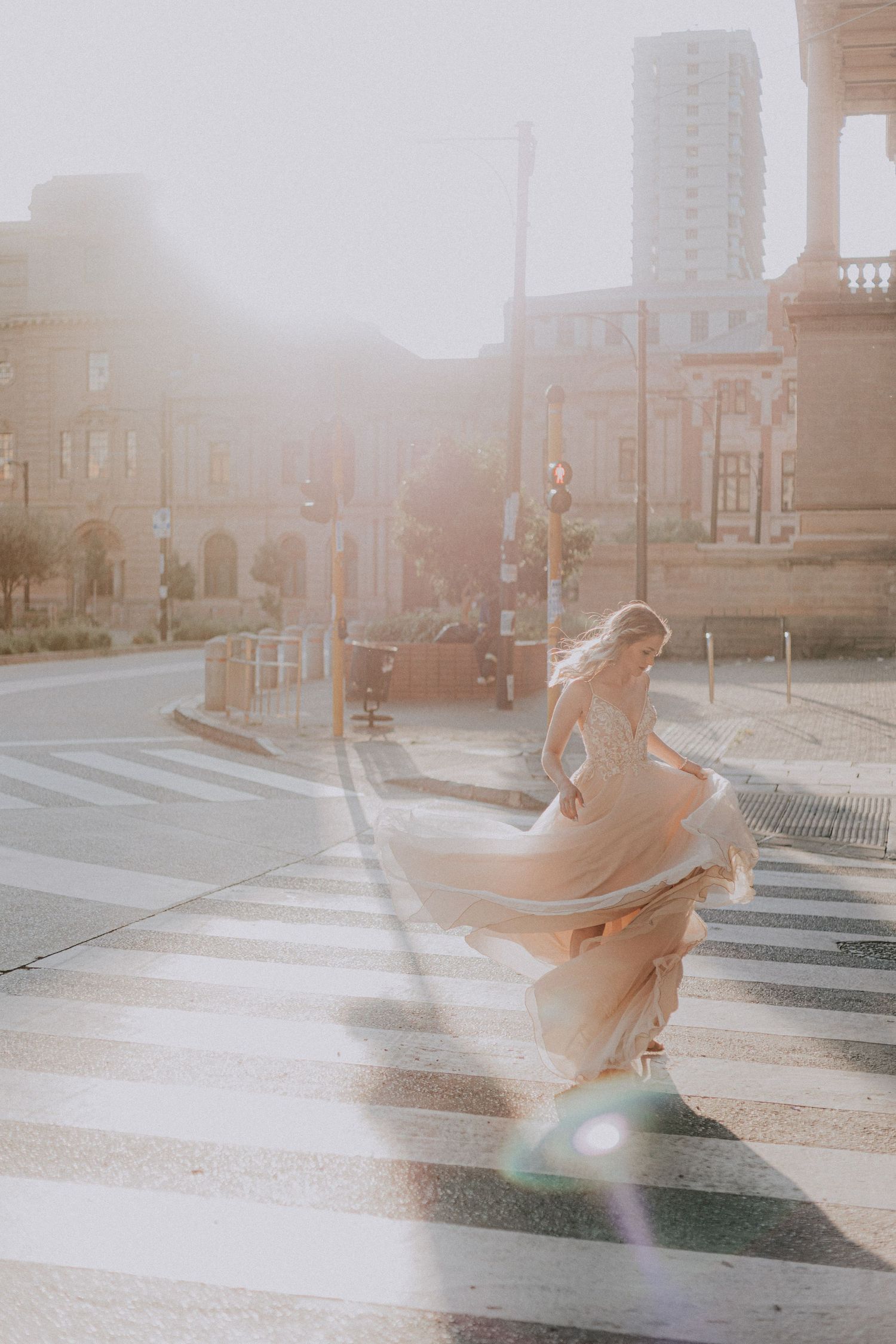 A flowing dress twirls gracefully in golden sunlight on a city crosswalk.