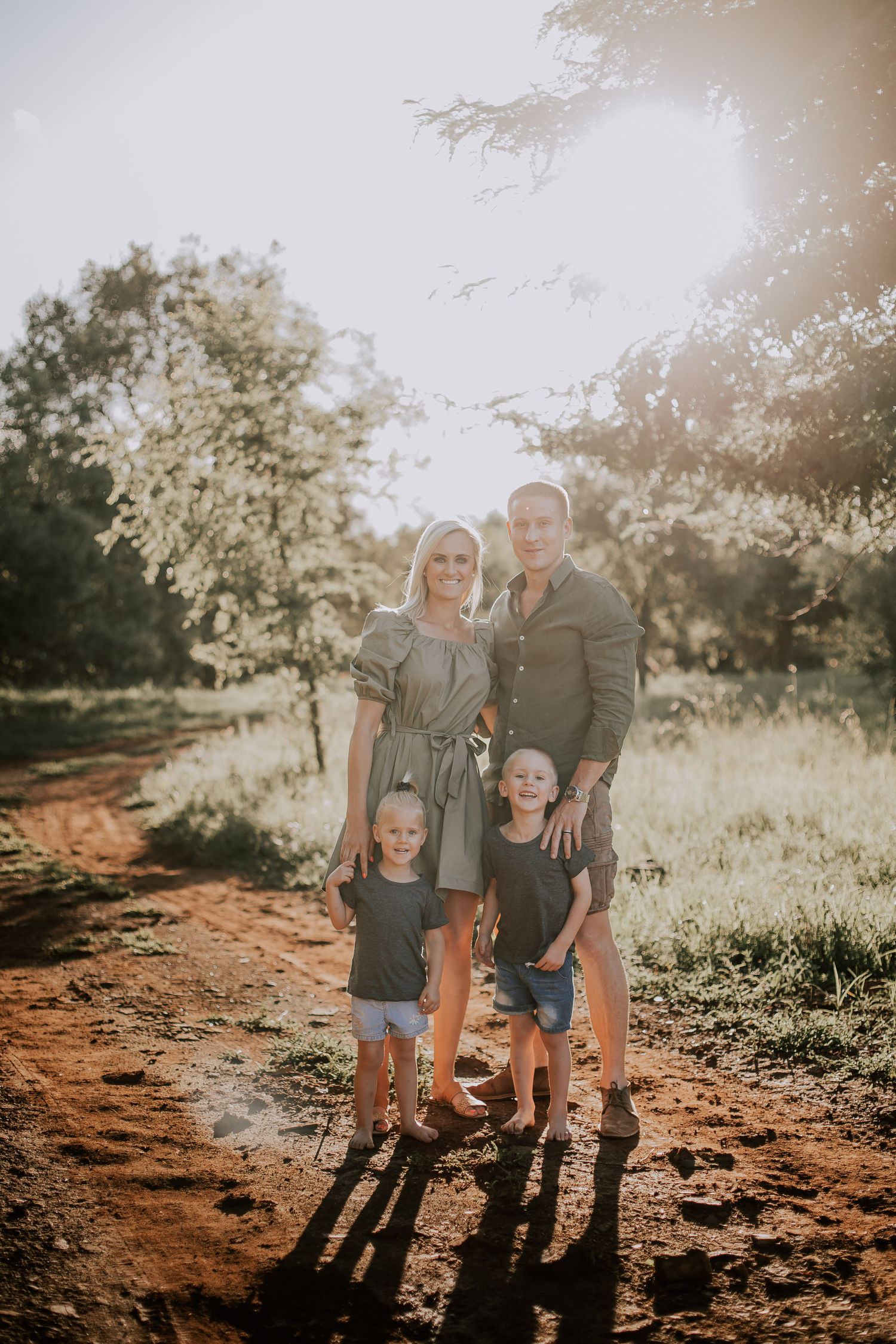 A family of four poses together on a dirt path during sunset creating long shadows behind them.