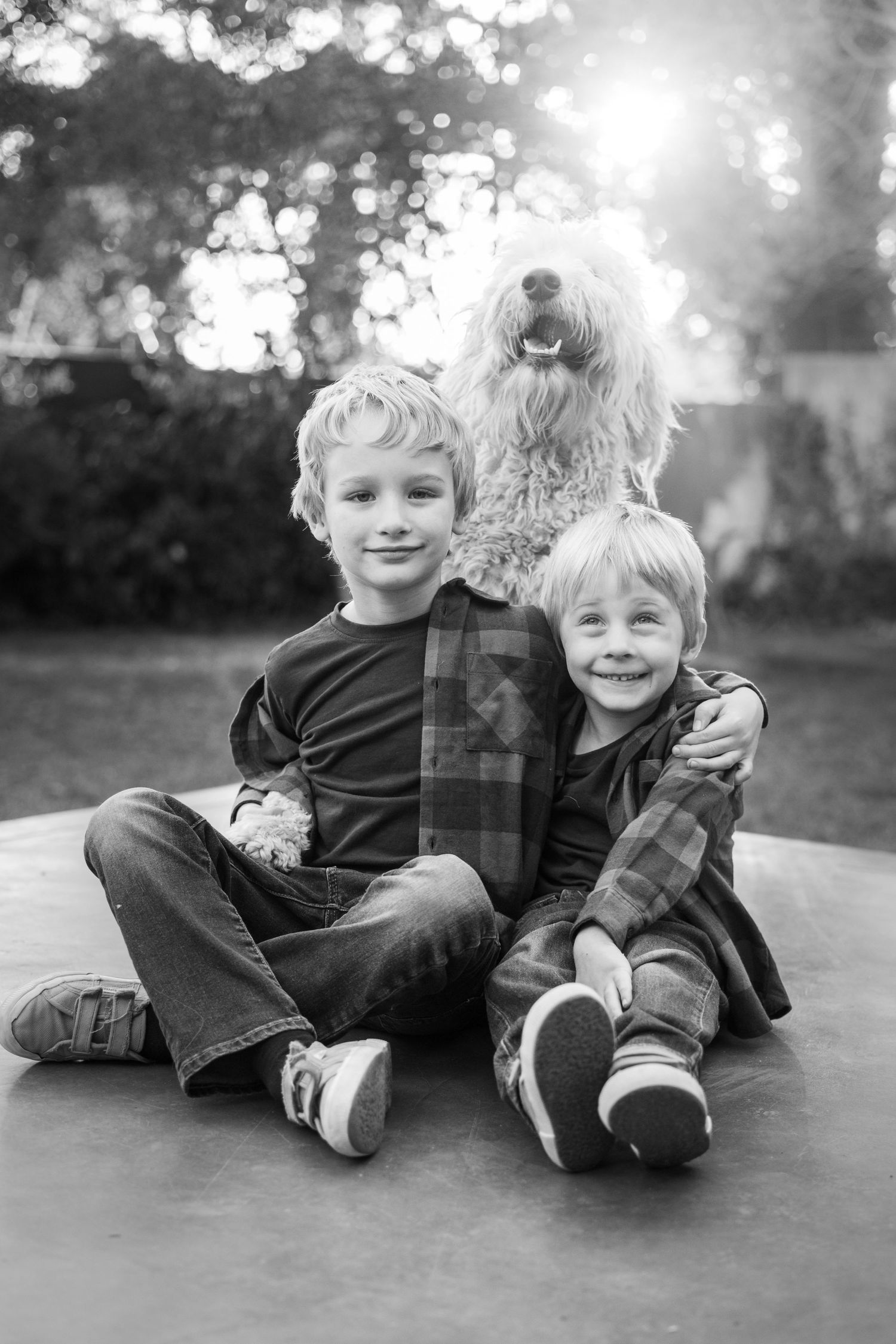 Two smiling children sitting with a fluffy dog in a black and white portrait.