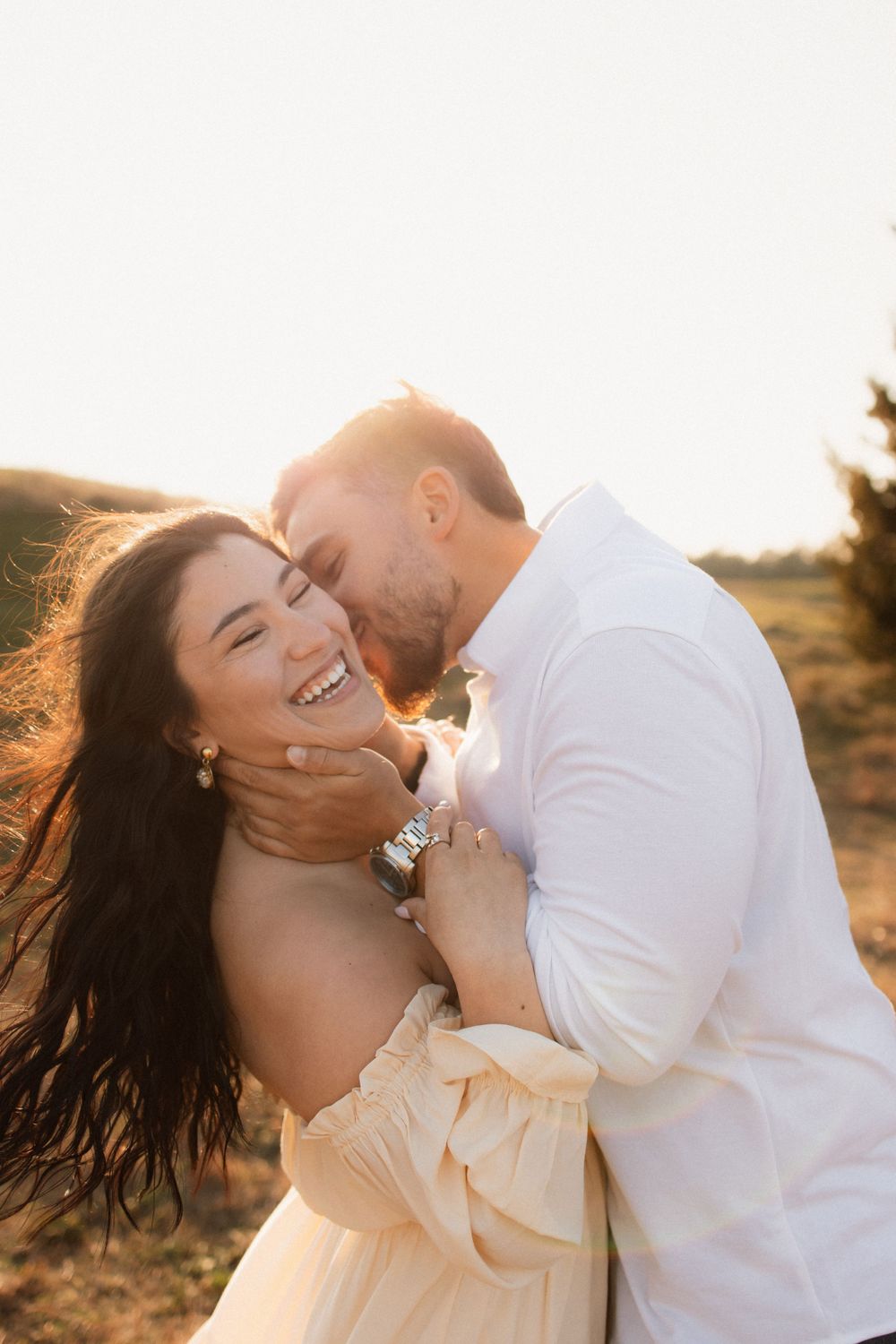 Couple sharing an intimate playful moment at sunset with warm backlight and joyful expressions.