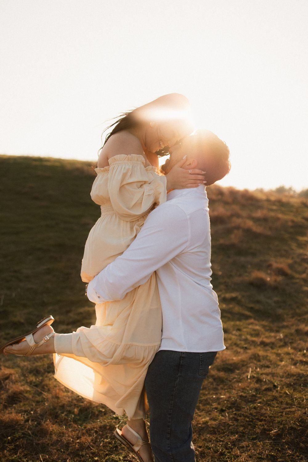 Couple embraces and twirls during golden hour photography session on hillside.