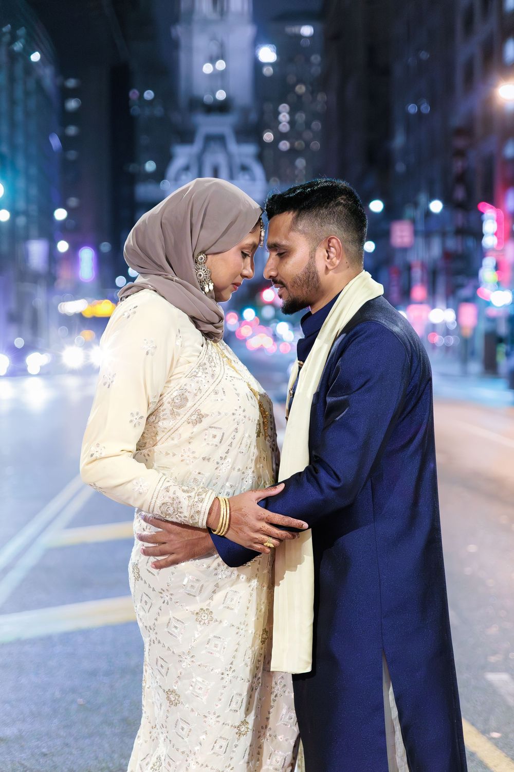 South Asian couple in traditional wedding attire sharing a romantic moment on a city street at night.