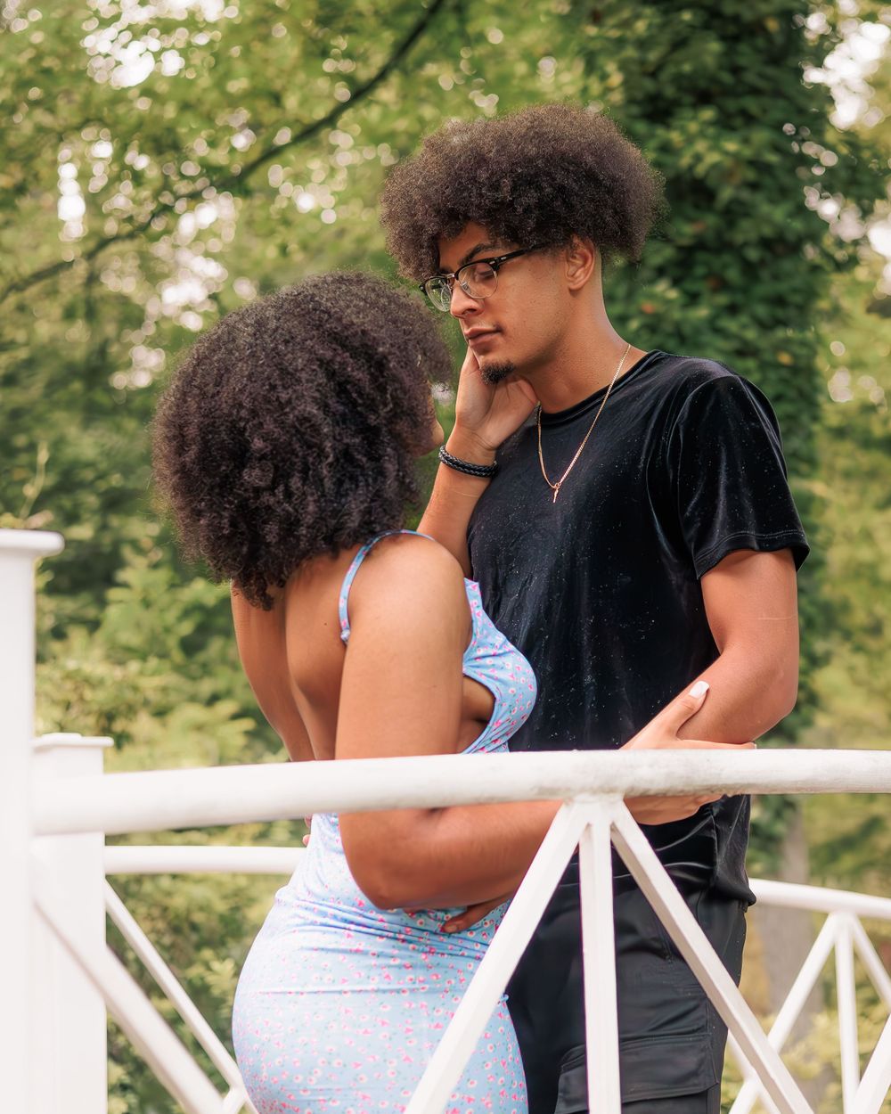 Young Black couple with natural curly hair share an intimate moment on a white bridge outdoors.